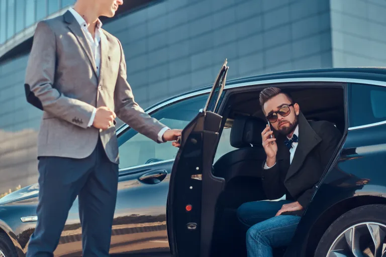 Business executive stepping out of a luxury car with chauffeur assistance, representing premium car rental services in Dubai.