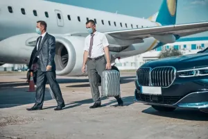 Traveler walking ahead while chauffeur carries luggage during luxury airport transfers from Dubai airport towards the car.