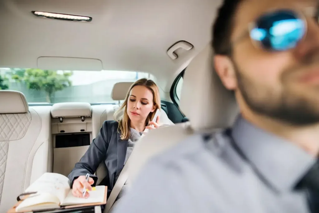Woman working inside a luxury car while a chauffeur drives in Dubai, highlighting the comfort of choosing a chauffeur over taxi.