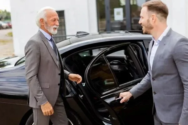 Luxury car chauffeur service Dubai showing an RTA-certified chauffeur opening the door of a premium black sedan for a businessman near Downtown Dubai in 2025