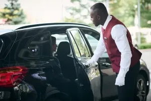 Professional chauffeur standing by the car door, looking inside at a seated client during a Dubai to Abu Dhabi car with driver transfer